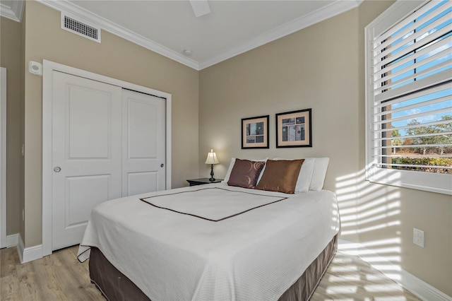 bedroom with baseboards, visible vents, ornamental molding, light wood-type flooring, and a closet