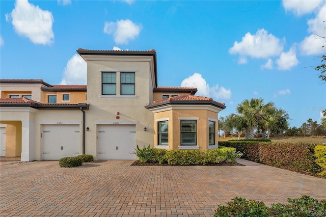 mediterranean / spanish house with driveway, a tiled roof, an attached garage, and stucco siding