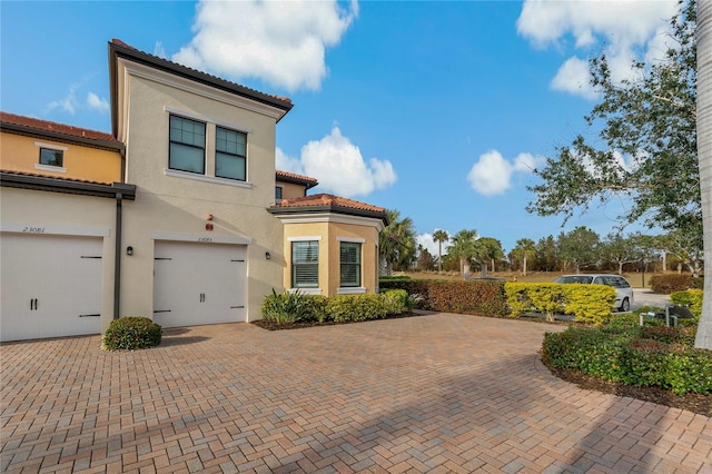 view of front facade featuring a garage, a tile roof, driveway, and stucco siding