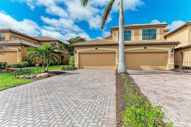 mediterranean / spanish house featuring a garage, a tile roof, decorative driveway, and stucco siding