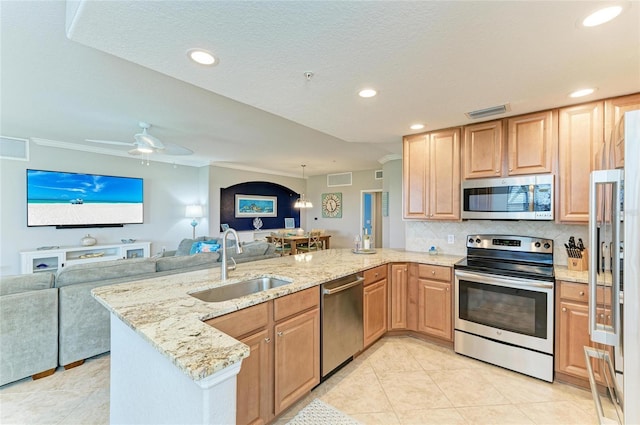 kitchen with light stone counters, appliances with stainless steel finishes, open floor plan, a sink, and a peninsula