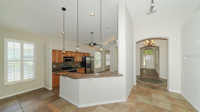 kitchen with arched walkways, appliances with stainless steel finishes, brown cabinetry, a kitchen bar, and pendant lighting