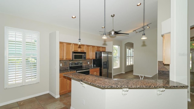 kitchen featuring a breakfast bar, hanging light fixtures, appliances with stainless steel finishes, dark stone countertops, and a peninsula