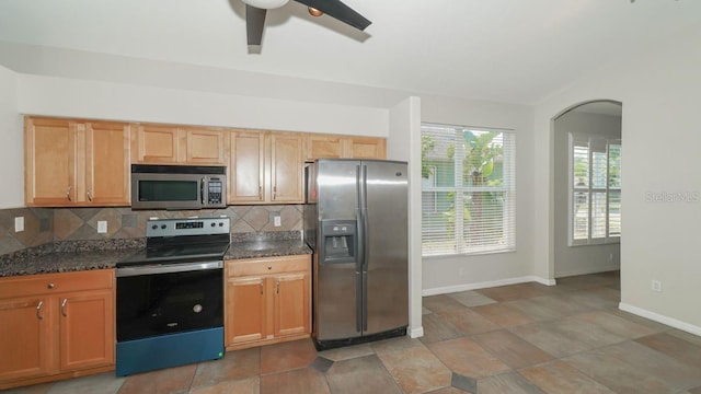 kitchen featuring stainless steel appliances, decorative backsplash, ceiling fan, dark stone counters, and baseboards