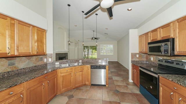 kitchen featuring appliances with stainless steel finishes, a sink, a peninsula, and dark stone countertops