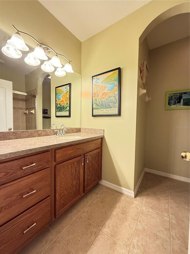 full bath featuring a tile shower, tile patterned flooring, vanity, and baseboards