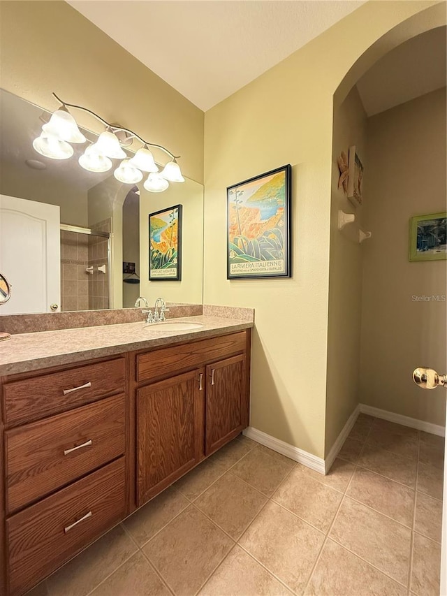 bathroom featuring tile patterned flooring, baseboards, tiled shower, and vanity