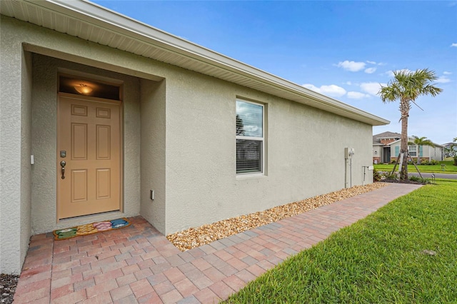 view of exterior entry featuring a yard and stucco siding