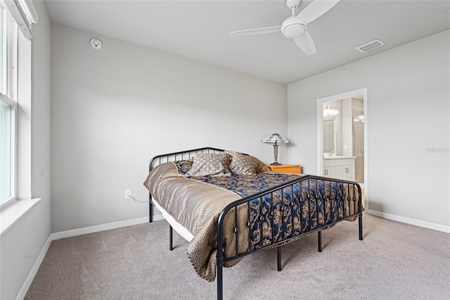 carpeted bedroom with a ceiling fan, ensuite bath, visible vents, and baseboards