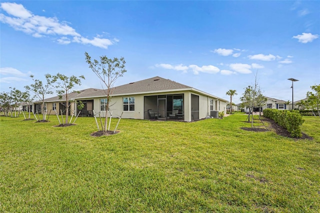 rear view of property featuring central air condition unit, a sunroom, a lawn, and stucco siding