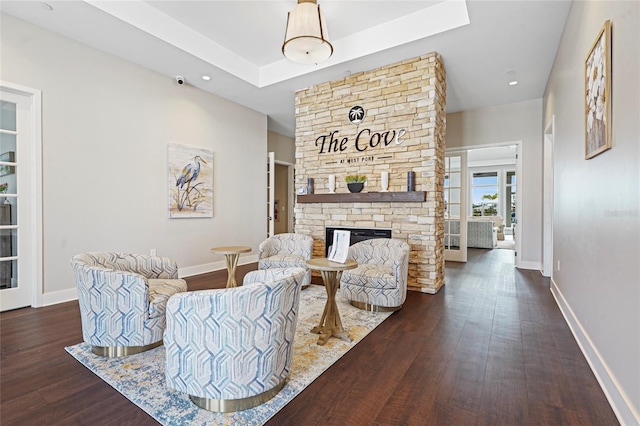 living area with a tray ceiling, a fireplace, wood finished floors, and baseboards