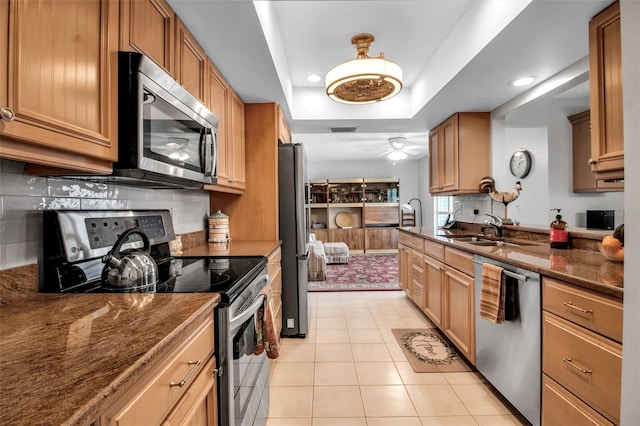 kitchen featuring light tile patterned floors, tasteful backsplash, appliances with stainless steel finishes, a tray ceiling, and a sink