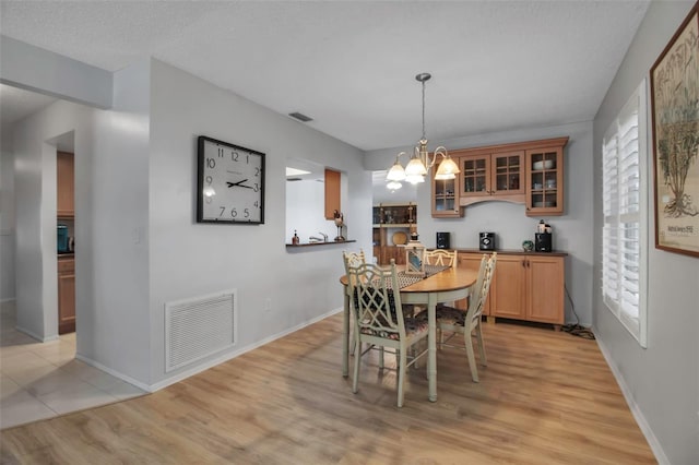 dining room featuring a chandelier, light wood-style flooring, visible vents, and baseboards