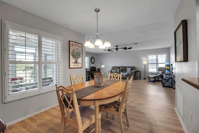 dining area with a textured ceiling, baseboards, light wood-style flooring, and a notable chandelier