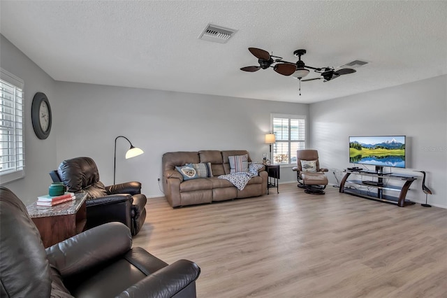 living room featuring a textured ceiling, ceiling fan, light wood-type flooring, and visible vents