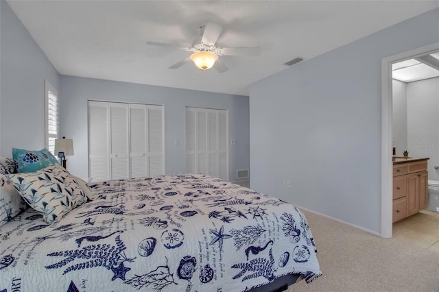 bedroom with light carpet, a ceiling fan, visible vents, multiple closets, and ensuite bath