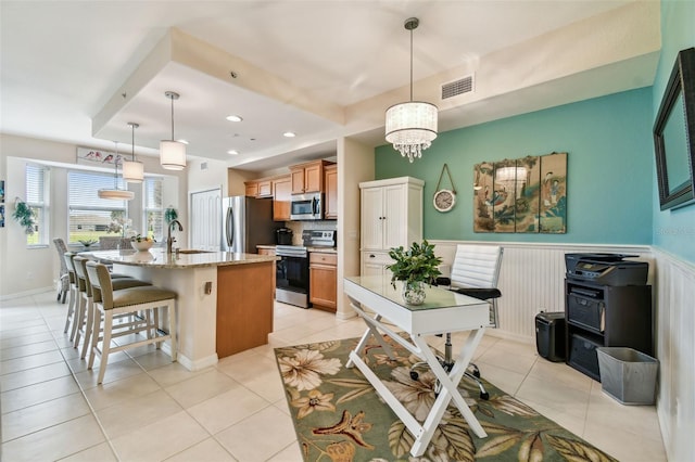 kitchen featuring light stone counters, a wainscoted wall, appliances with stainless steel finishes, a sink, and a kitchen breakfast bar