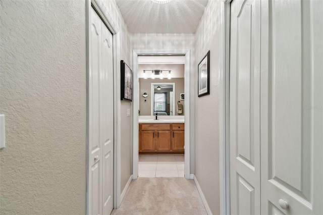 hall featuring light tile patterned floors, light colored carpet, a textured wall, a sink, and baseboards