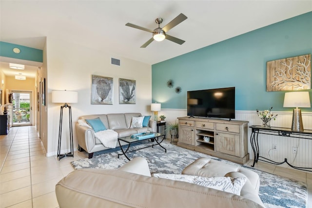 living room with a wainscoted wall, ceiling fan, light tile patterned flooring, and visible vents