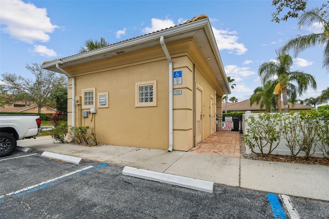 view of home's exterior with uncovered parking, a gate, fence, and stucco siding