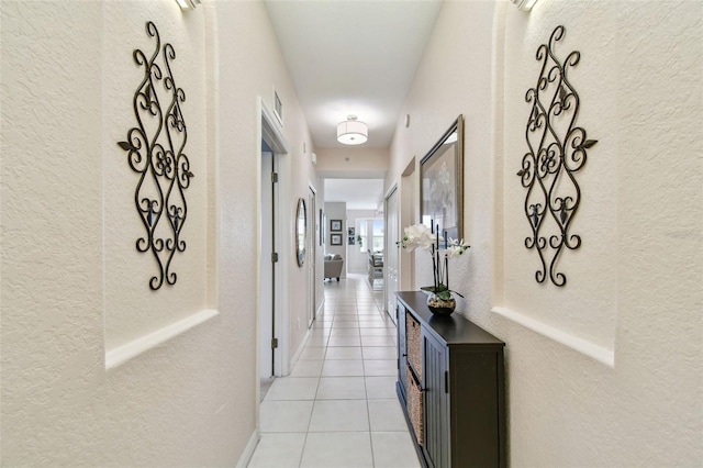 hallway featuring light tile patterned floors, baseboards, visible vents, and a textured wall