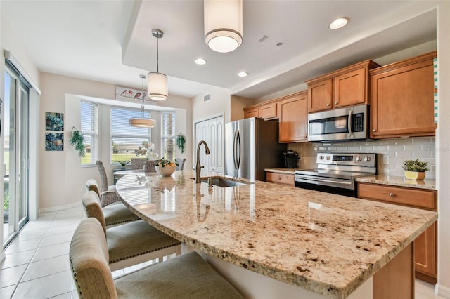 kitchen with a breakfast bar area, a center island with sink, a sink, stainless steel appliances, and backsplash