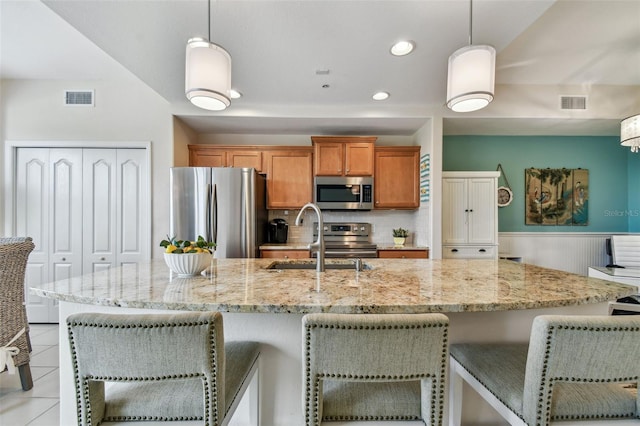 kitchen featuring visible vents, brown cabinets, stainless steel appliances, a kitchen bar, and a sink