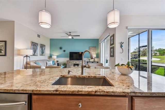 kitchen featuring open floor plan, light stone counters, a sink, and pendant lighting