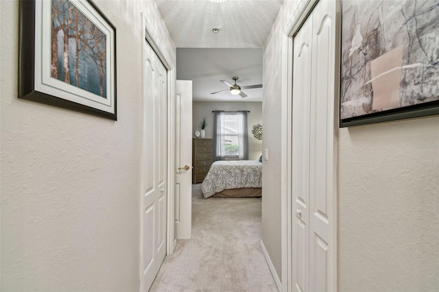 hallway with a textured ceiling, a textured wall, carpet, and baseboards