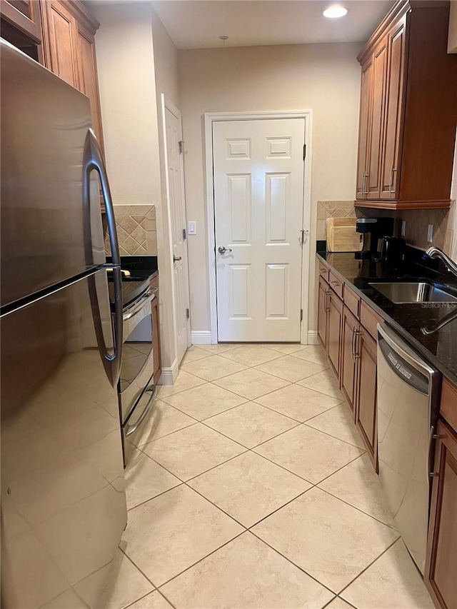 kitchen featuring decorative backsplash, brown cabinets, dark stone countertops, stainless steel appliances, and a sink