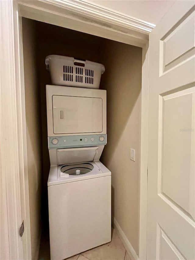 clothes washing area featuring stacked washer and dryer, light tile patterned floors, and baseboards