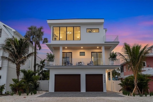 contemporary home featuring decorative driveway, fence, a balcony, and stucco siding