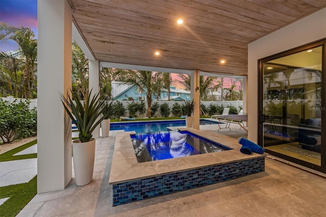 pool at dusk with a fenced in pool, a patio, a hot tub, and fence