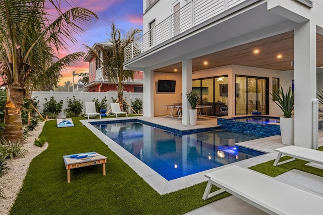 pool at dusk featuring a fenced in pool, a patio, a lawn, a hot tub, and fence