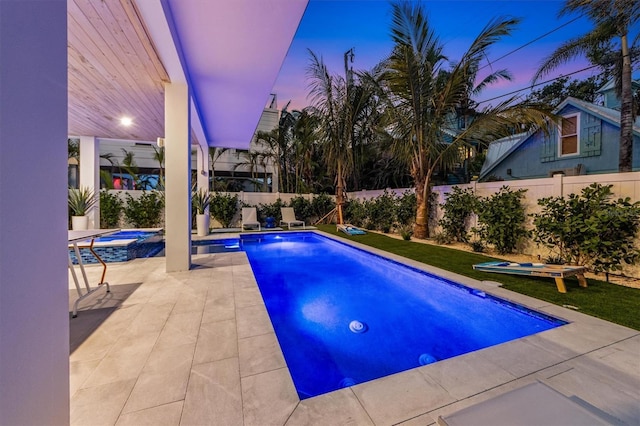 pool at dusk with a fenced in pool, a patio area, a fenced backyard, and an in ground hot tub