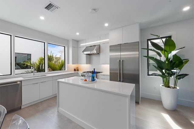 kitchen featuring a sink, white cabinets, light countertops, appliances with stainless steel finishes, and wall chimney exhaust hood