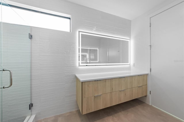 full bath featuring a stall shower, wood finished floors, vanity, and tile walls