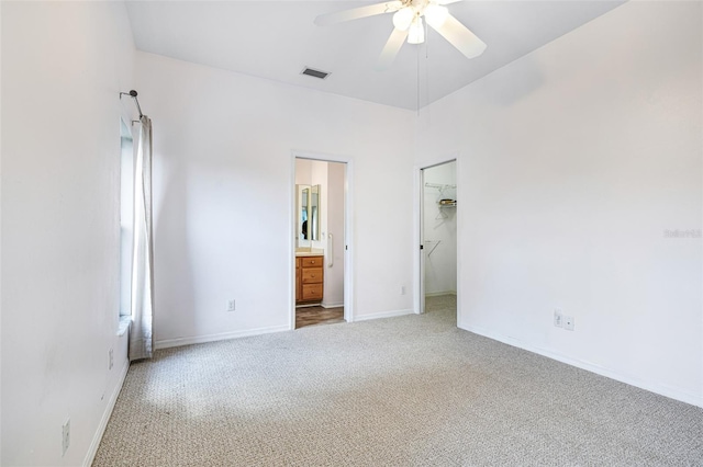 unfurnished bedroom with light carpet, a spacious closet, ensuite bath, and baseboards