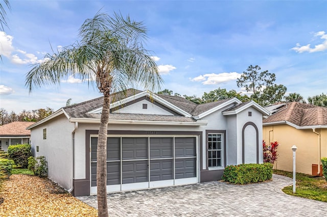 ranch-style house featuring decorative driveway, an attached garage, and stucco siding