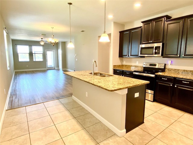 kitchen featuring light stone counters, light tile patterned flooring, stainless steel appliances, a sink, and a center island with sink