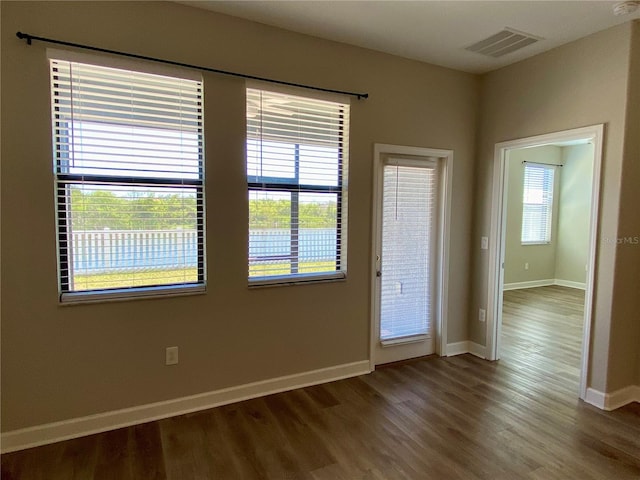 spare room featuring visible vents, plenty of natural light, baseboards, and wood finished floors