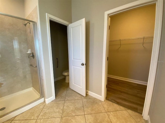 bathroom with a spacious closet, toilet, a stall shower, baseboards, and tile patterned floors