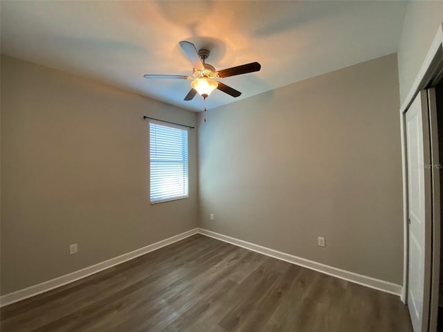 empty room with dark wood-style flooring, a ceiling fan, and baseboards