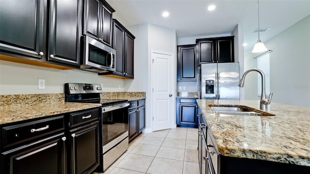 kitchen featuring dark cabinetry, appliances with stainless steel finishes, a sink, and light stone counters