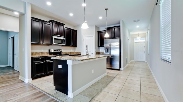kitchen featuring visible vents, a kitchen island with sink, light stone countertops, a sink, and stainless steel appliances