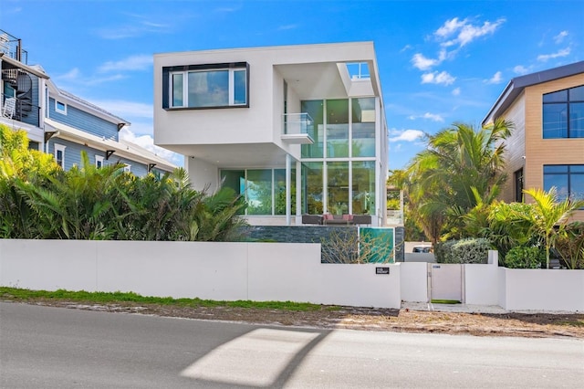 contemporary house featuring a balcony, a fenced front yard, and stucco siding