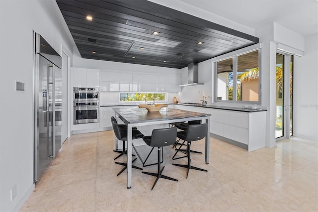 kitchen with white cabinets, wall chimney range hood, appliances with stainless steel finishes, dark countertops, and modern cabinets