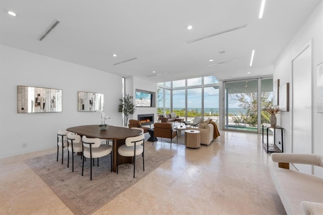 dining room featuring a wall of windows, a wealth of natural light, a warm lit fireplace, and visible vents