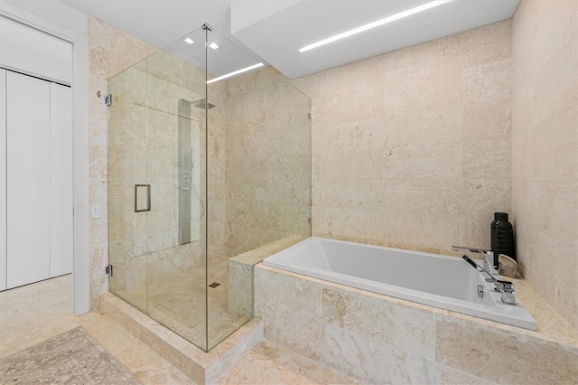 full bathroom featuring a shower stall, a bath, and tile walls