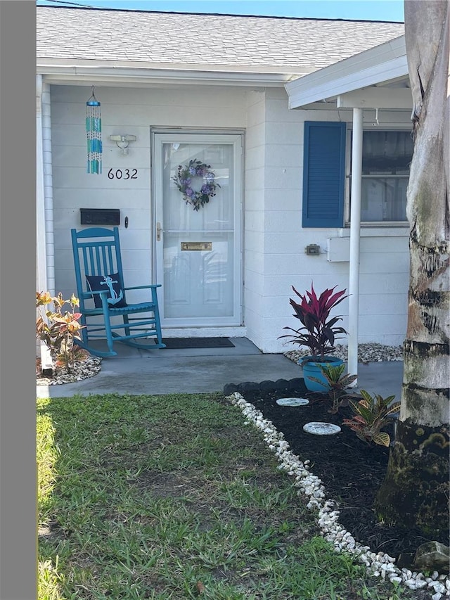 doorway to property featuring a shingled roof, concrete block siding, and a porch